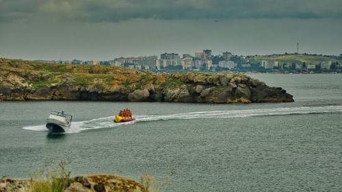 A speedboat towing people on a banana boat near the shore
