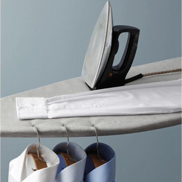 An iron resting on an ironing board next to crisp collared shirts hanging neatly underneath.