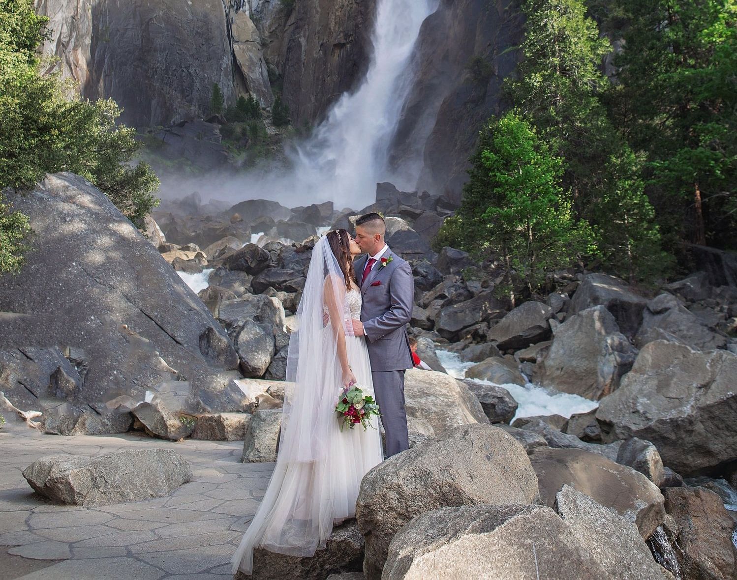 A couple posing for a wedding photoshoot in front of a waterfall in Yosemite - Narrow Gauge Inn - A Serenite Hotel Near Fish Camp.
