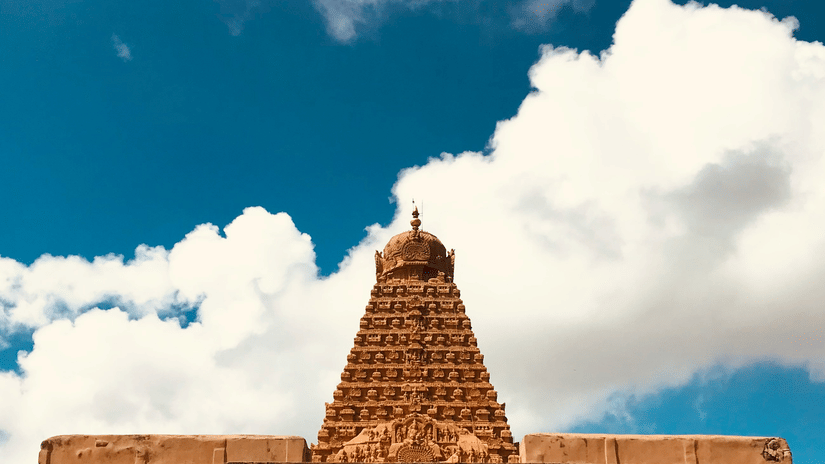 A section of the temple architecture is visible beneath a bright blue sky filled with white, fluffy clouds.