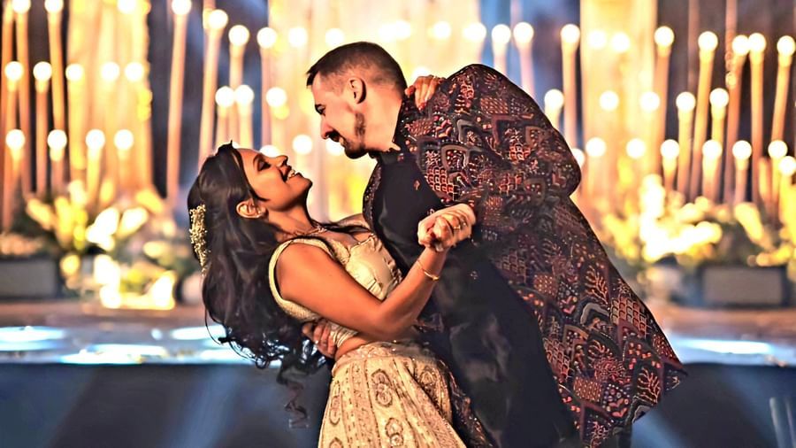 A couple dances intimately on a stage illuminated by spotlights, surrounded by decorative lighting in a celebratory setting