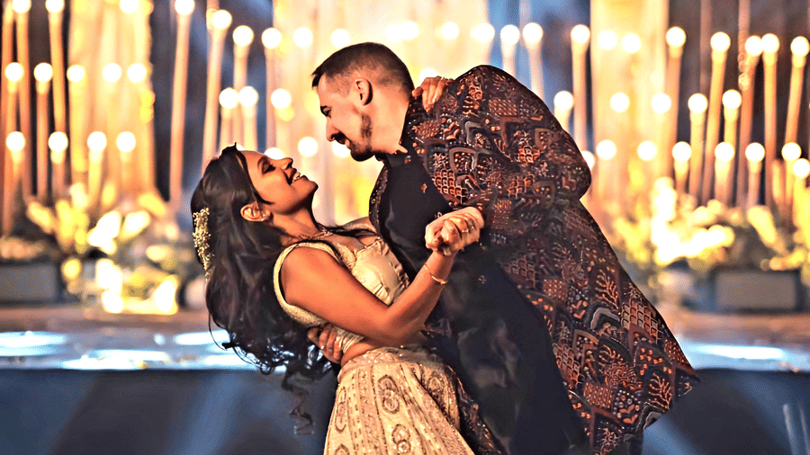 A couple sharing a romantic dance moment at a wedding celebration at Vedic Village Spa Resort with dramatic stage lighting and a floral decorated backdrop in the background.
