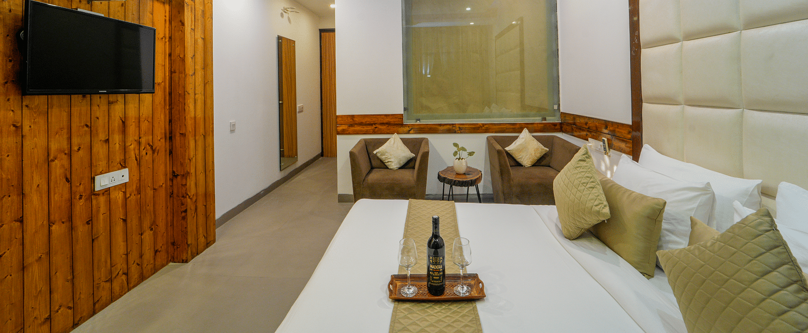 An image of the premium room with a bed, two single sofa chairs, a flat screen TV, and air-conditioning - DLS Whispering Winds