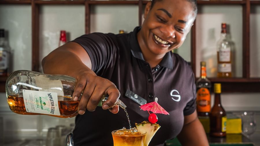 A bartender pouring a cocktail into a glass containing  a fruit peel and a cocktail umbrella - S Hotel Montego Bay, Jamaica