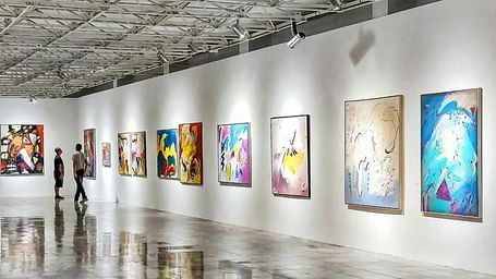 A brightly lit art gallery with white walls and several framed pieces displayed along the length of the room.