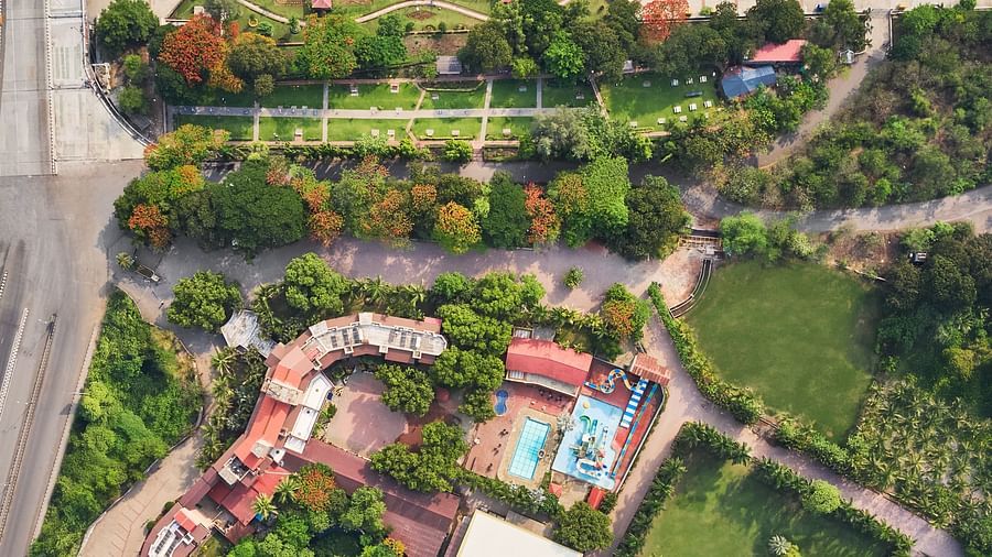 Aerial view of DGV Resort by Treat, Silvassa by a waterfront, featuring landscaped gardens, swimming pool, lawns, walking paths, and red-roofed buildings.