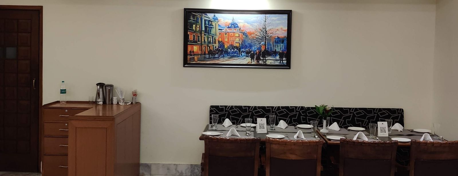 The dining area at the Gold Plate restaurant with a dining table with set cutlery on it along with a wall mounted photo frame - Hotel Gold, Panipat
