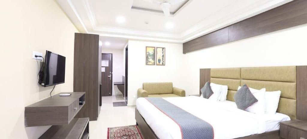 Full view shot of a brightly lit Premium Room at Pravasa Ahmedabad featuring a double bed and a wall mounted television placed opposite to it.