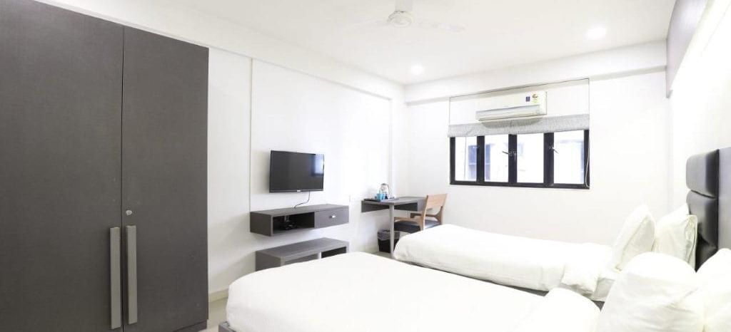 Corner view shot of the Premium Twin Room at Pravasa Ahmedabad featuring bright and minimalist interiors along with a wardrobe in the corner.