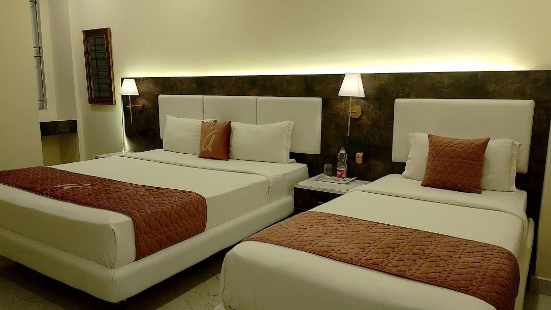 A spacious hotel room with a double bed and a single bed, matching brown bed runners, warm lighting, and a minimalist design - Astra Hotels and Suites, HSR Sector 7