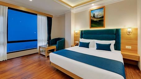 An image of the premium room with bed, bed side table, sofa, table and window overlooking the view - Yashshree Sikkim Blossom, Gangtok
