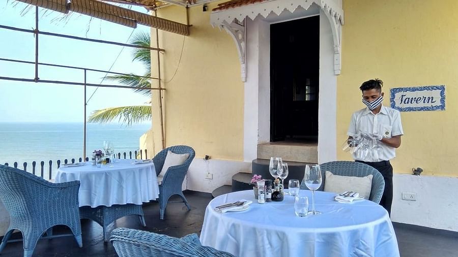 An indoor restaurant area at Fort Tiracol, Goa, with tables set with white tablecloths and wicker chairs.