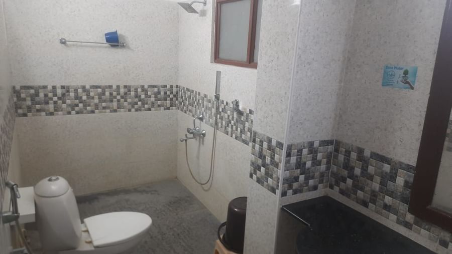 Bathroom at Udipi Home, Egmore, Chennai featuring a wall-mounted toilet, handheld shower, and patterned wall tiles.