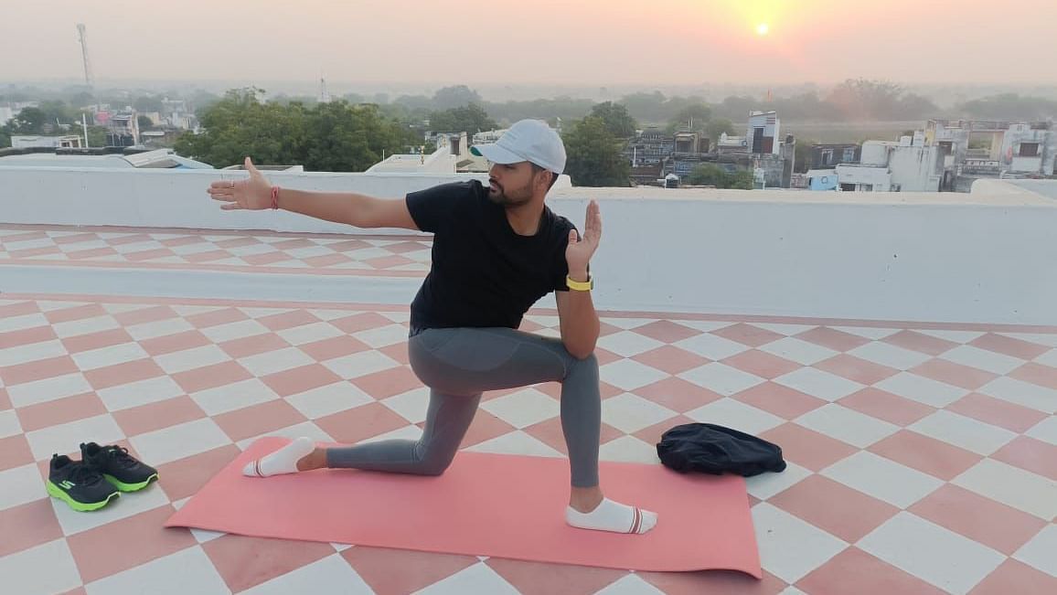 A person performs a yoga pose on a mat on a rooftop with a sunrise or sunset in the background.