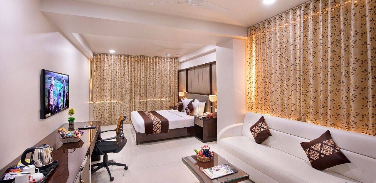 A well-appointed hotel room features two neatly made single beds, a work desk with a chair, and a wall-mounted television.