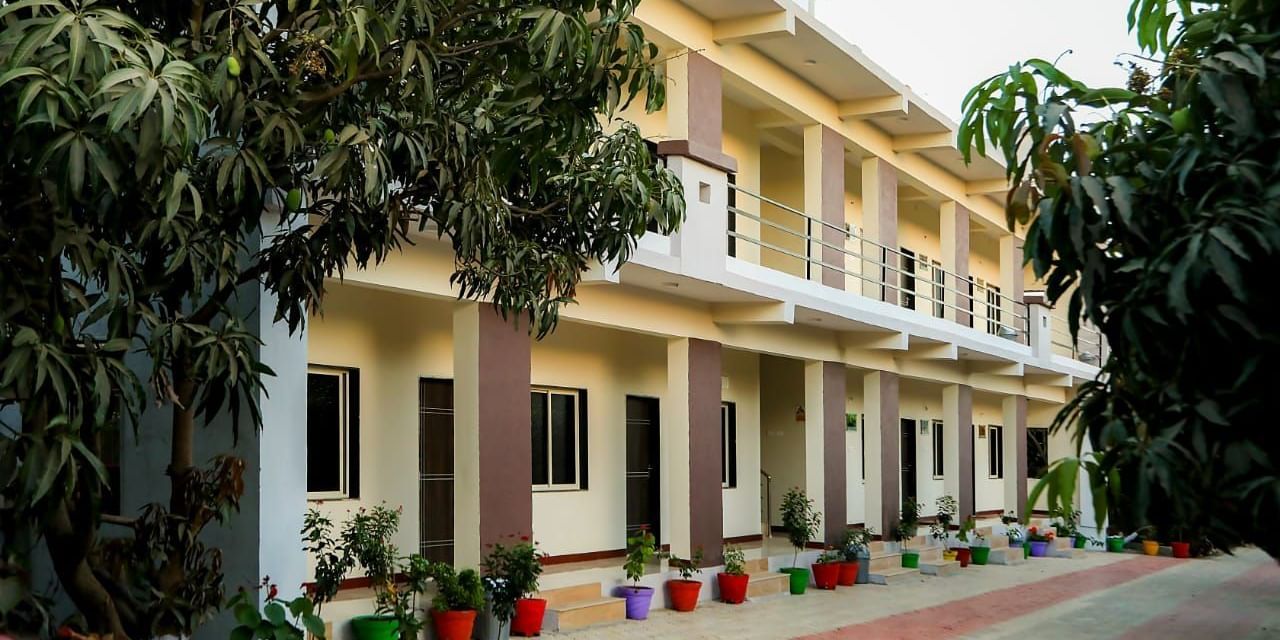 Exterior view of a two-storey building with potted plants and paved path at Daksh Resort & Amusement Park.