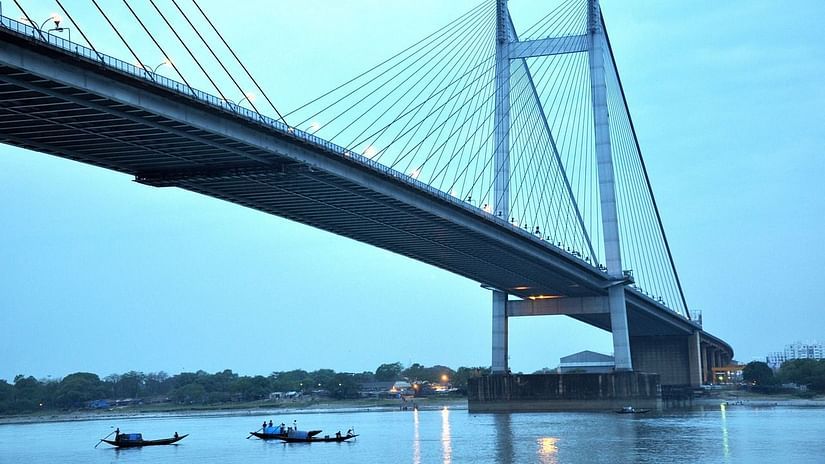 Large suspension bridge spanning over a calm river with boats underneath at twilight.
