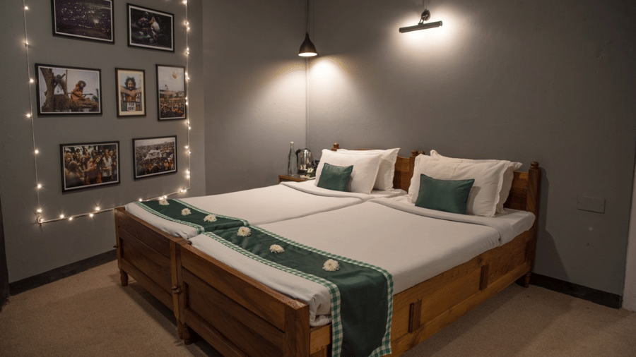 A hotel bedroom with twin wooden beds, white linens, matching runners, framed photo wall, and warm ambient lighting.