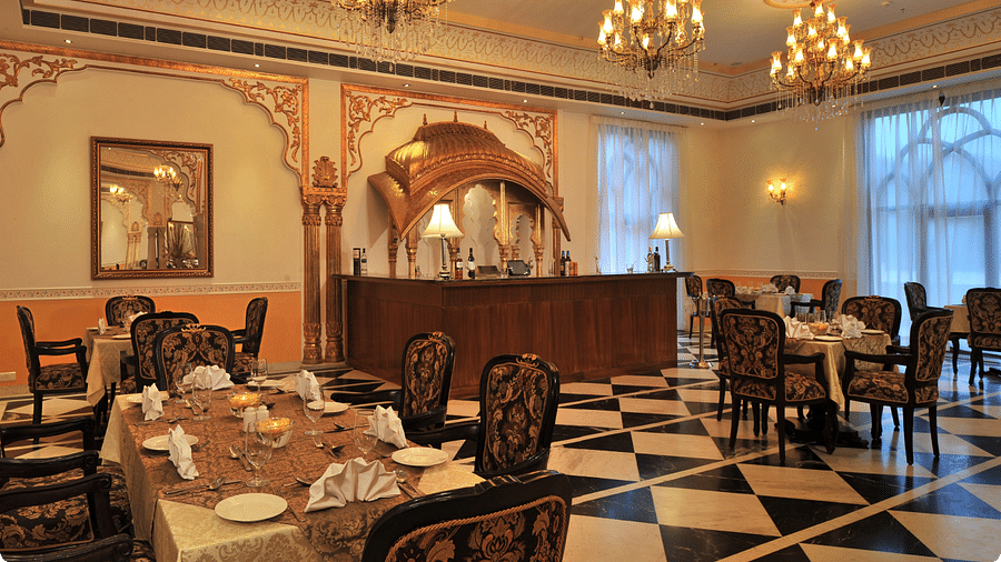 Dining area at Rajasthali Resort & Spa Jaipur with chairs, tables and chandeliers hanging from the ceiling.