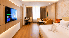 A Suite view at Pride Premier Greater Noida showing a double bed with towel art, a flat-screen television, and a separate lounge area in the background.