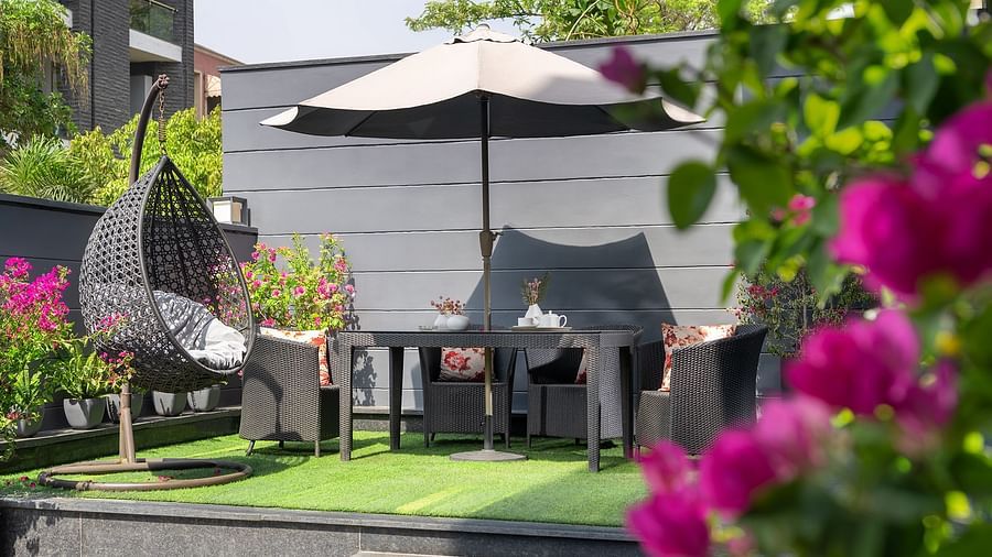 An inviting outdoor patio at The Atara, Gurugram featuring a dining set with an umbrella for shade, surrounded by vibrant blooming flowers and lush green foliage, perfect for relaxation