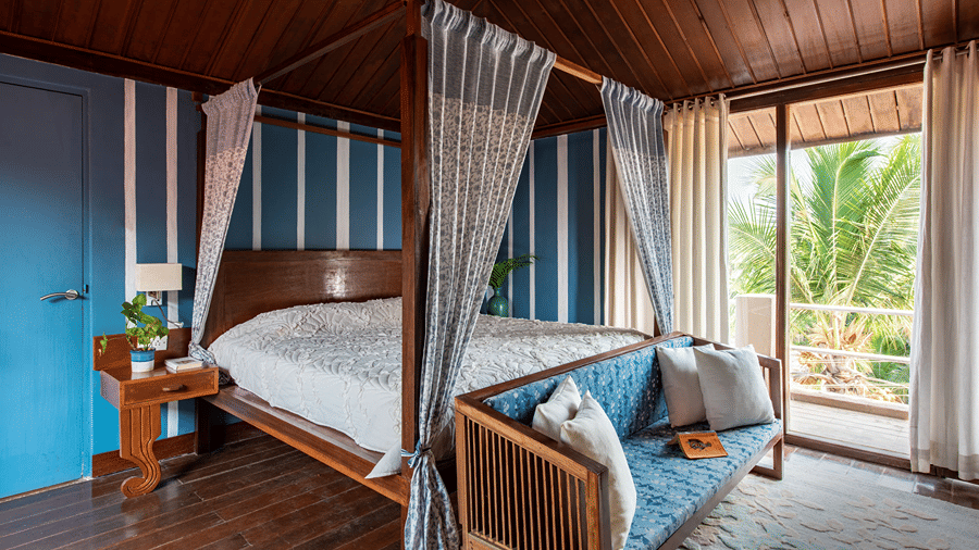 Four poster king size bed with white canopy curtains in a wood-panelled room overlooking greenery.