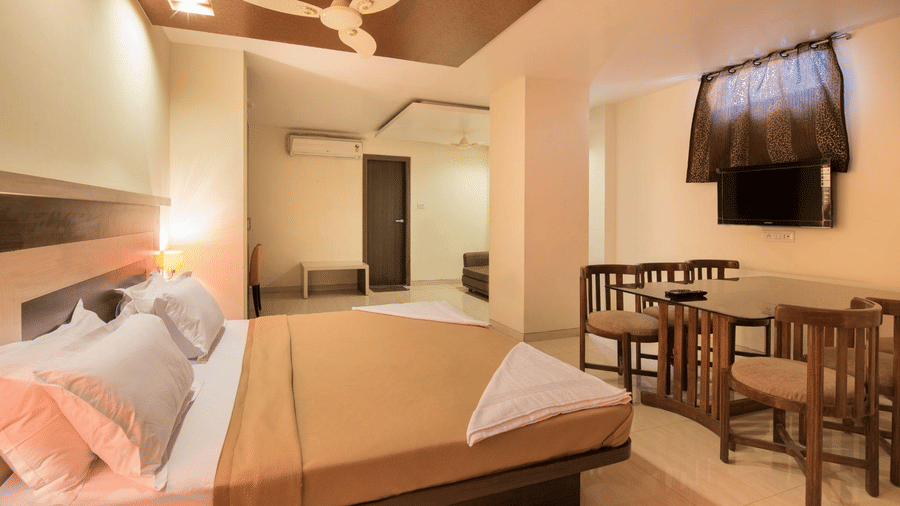 Well-furnished suite room with a double bed, ceiling fan, wall-mounted television, and a wooden table with chairs.