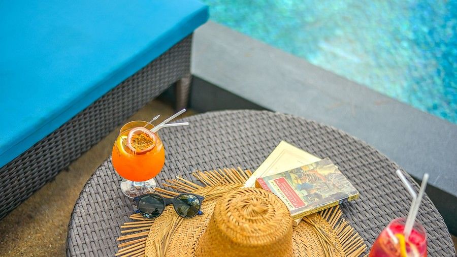 image of the table on the poolside with refreshing drinks, a straw hat, sunglasses and a book - Maikhao Dream Villa Resort & Spa, Phuket
