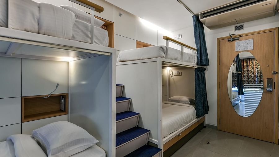 A pair of bunk beds with curtains pulled to the side, a staircase placed in the middle, bright lighting, and a wooden door with an oval-shaped mirror at Indie Stays, BKC Kalina.