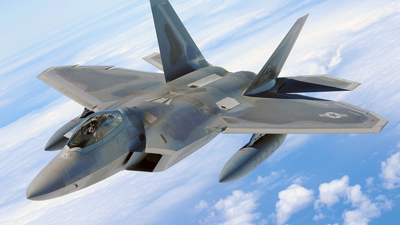 Aerial view of a stealth fighter jet banking through the sky above scattered white clouds.