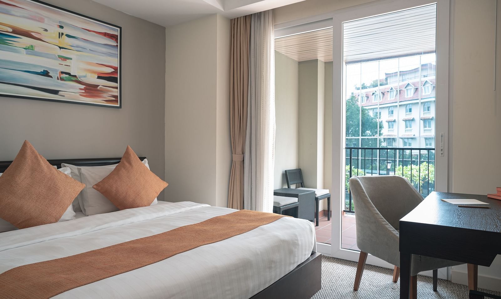 A bedroom with a bed, pillows, a nightstand, a table, a chair, and a window with a view | Three-bedroom Suite | Central Mansions, Phnom Penh