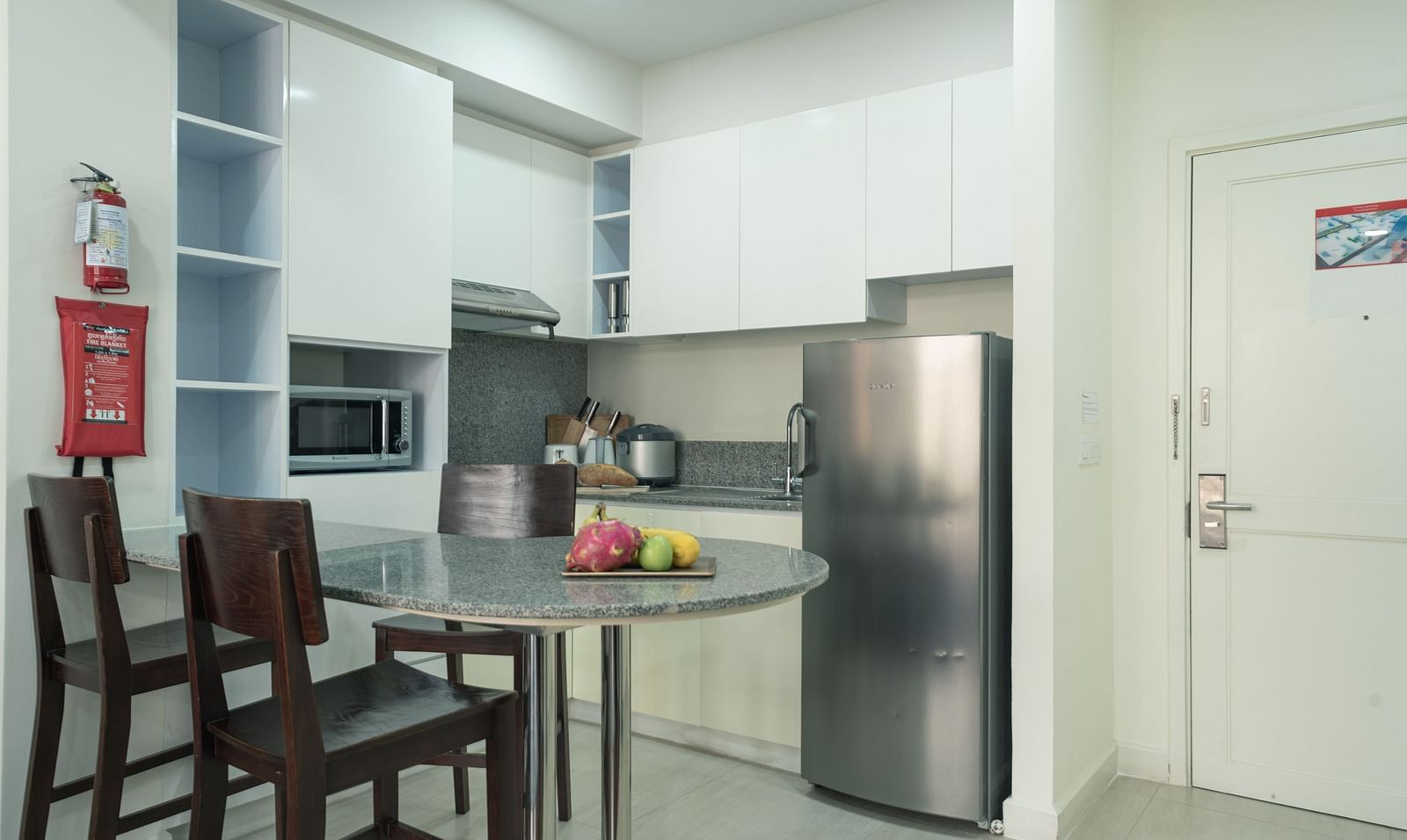 A kitchen with dark wood chairs, a table, a stainless steel refrigerator, and white cabinets | Two-bedroom Suite | Central Mansions, Phnom Penh