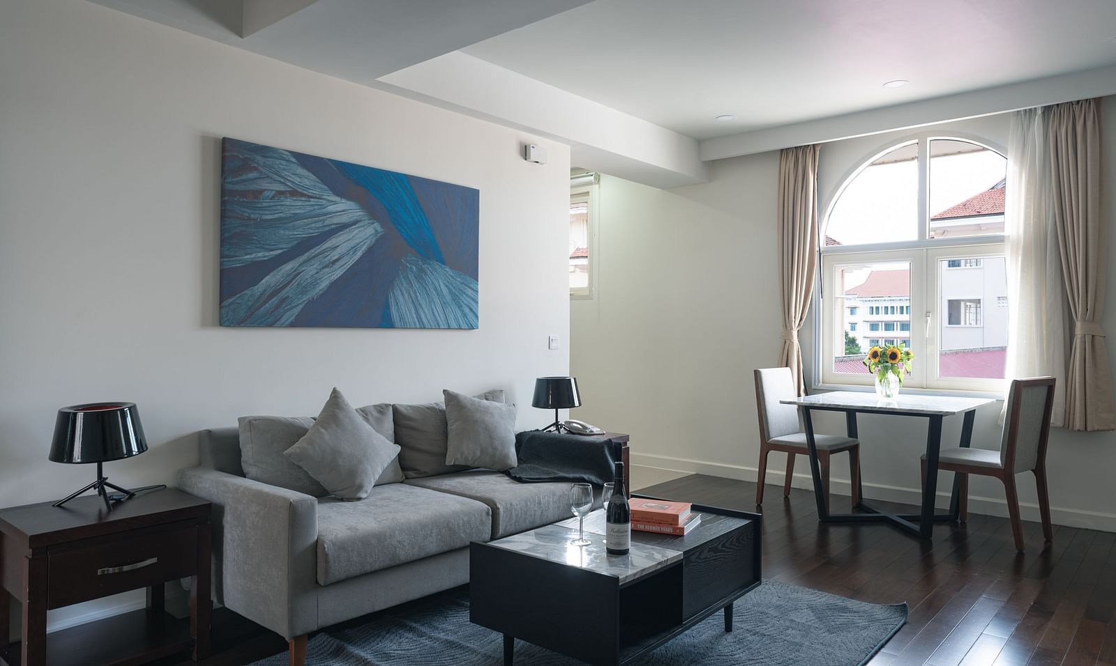 A living room with a grey sofa, a coffee table, and a dining table | One-bedroom Suite | Central Mansions, Phnom Penh