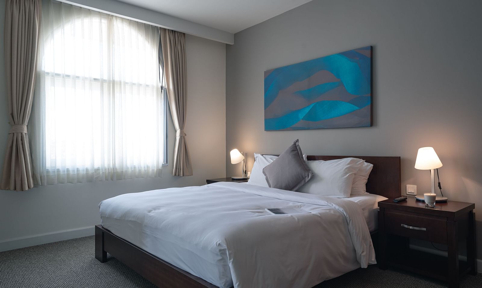 A well-lit bedroom with a large bed, a nightstand, and a modern painting above the headboard | One-bedroom Suite | Central Mansions, Phnom Penh