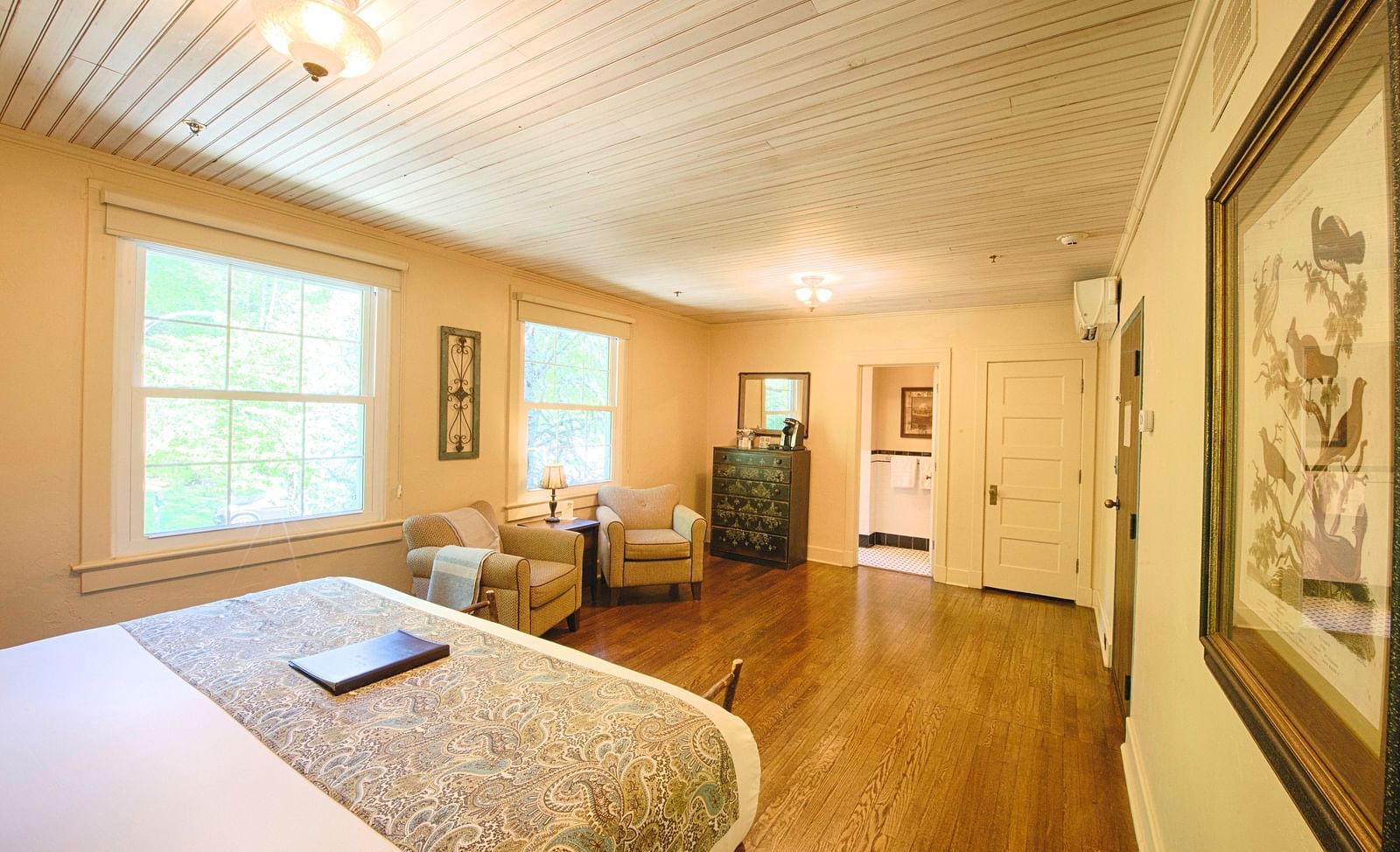 a brightly lit bedroom featuring a double bed with a file kept over it and with a comfortable seating area in front of it - Historic Tapoco Lodge