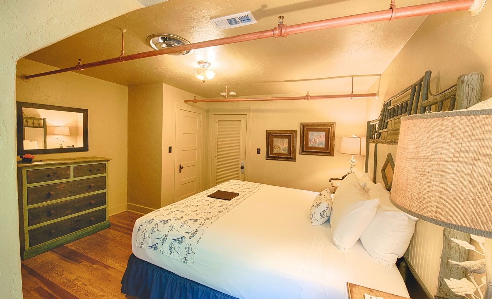 corner view image of the bedroom with two wide framed photos wall mounted in the corner and a wooden drawer in front of the bed - Historic Tapoco Lodge