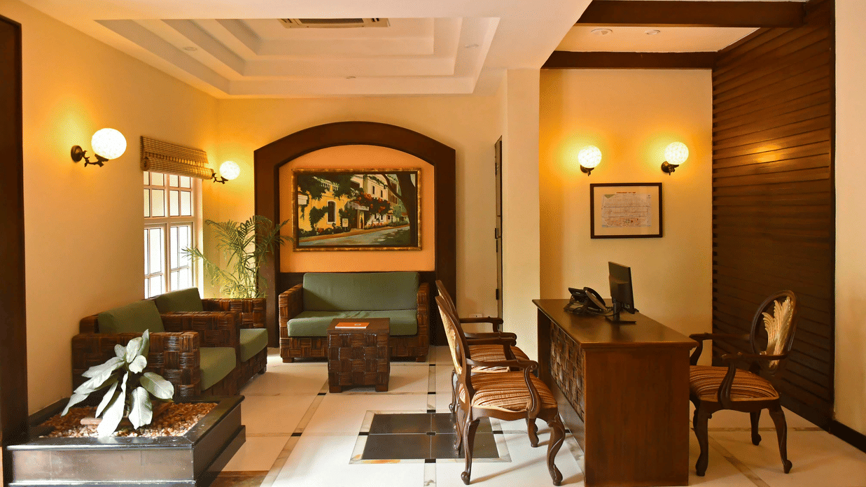 Reception lobby at The Richmond Puducherry featuring a desk with chairs, and a seating area with sofa set and a centre table.