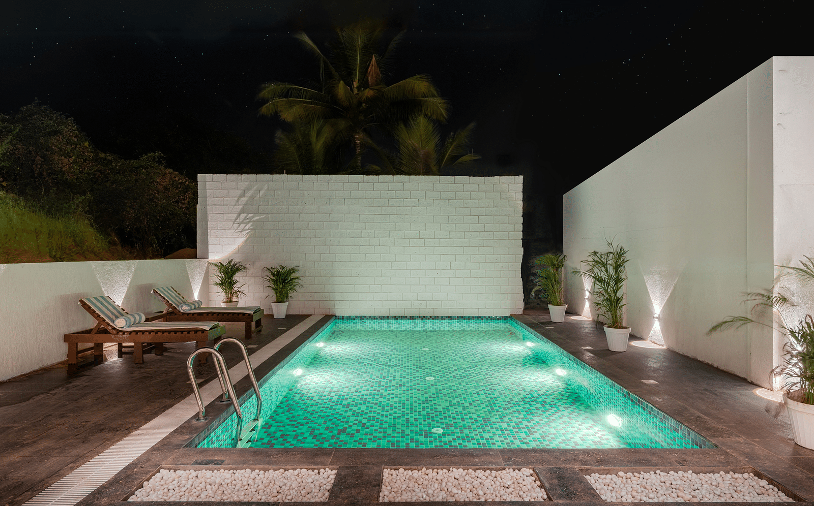 Outdoor pool area with green lighting and privacy walls at night at Bedzzz Xclusiv Morjim, Goa