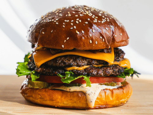 A gourmet burger with lettuce, cheese, and tomato served on a sesame bun, placed on a wooden surface