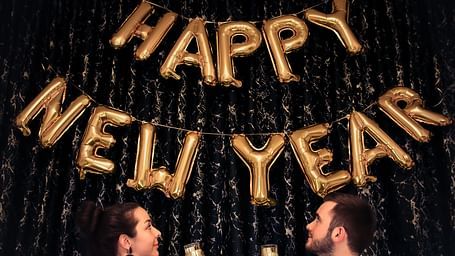 a couple holding a glass of champagne and looking at Happy New Year made out of ballons