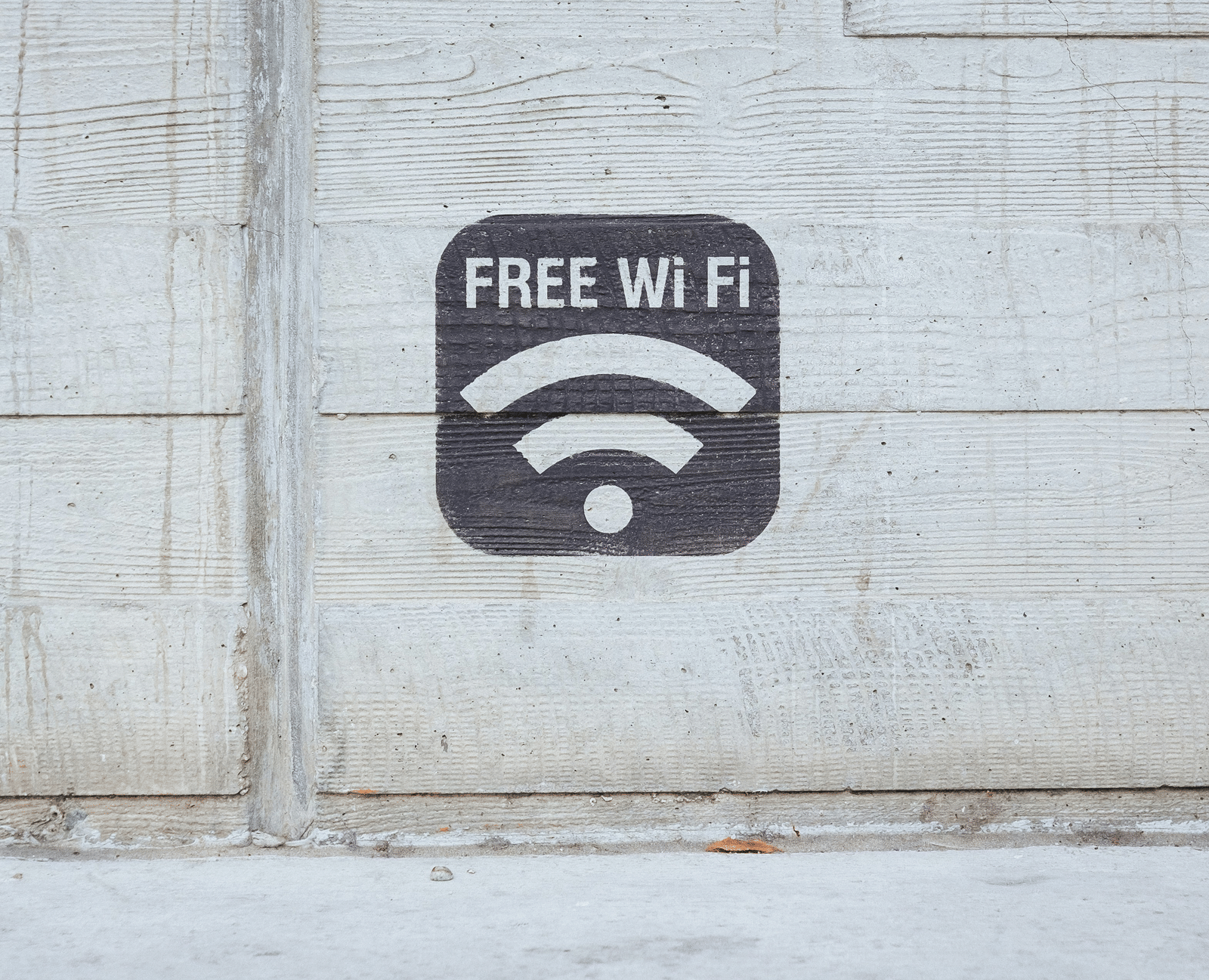 A close-up of a small, square sign with a standard Wi-Fi symbol, mounted on a textured grey wall.