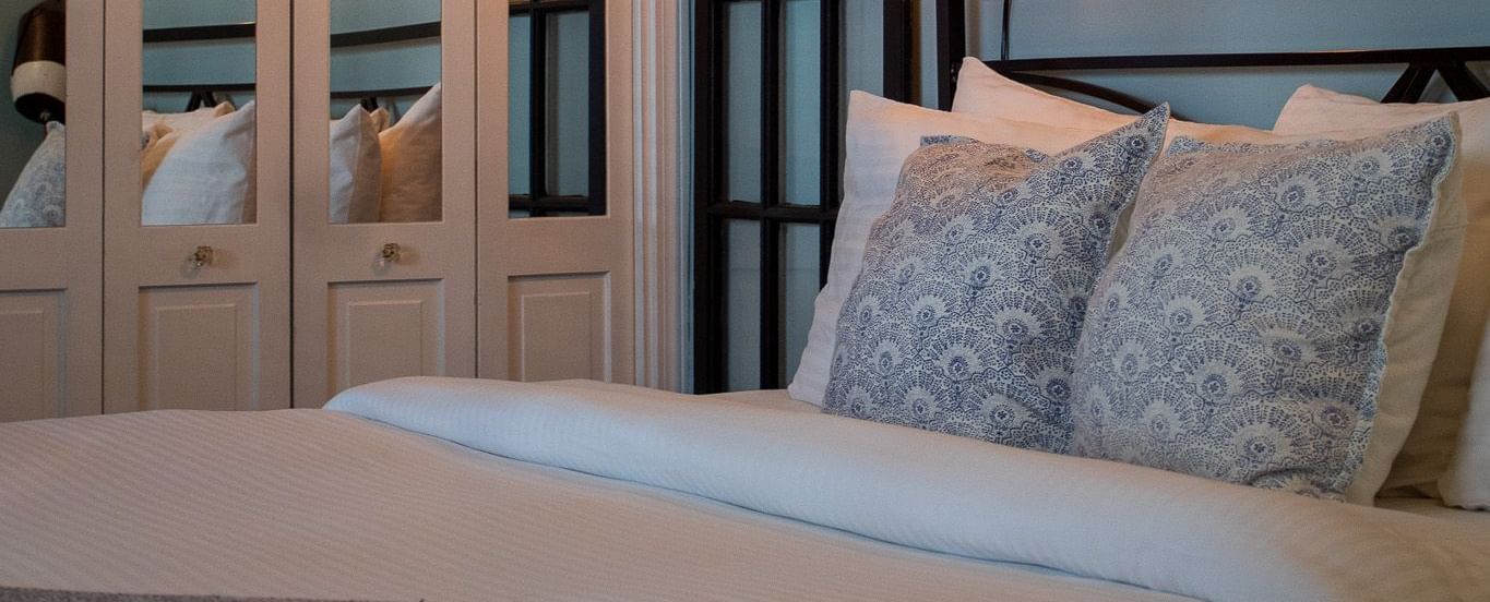 A bedroom with metal headboard, blue patterned pillows, maritime artwork and lantern sconces at Hartstone Inn.