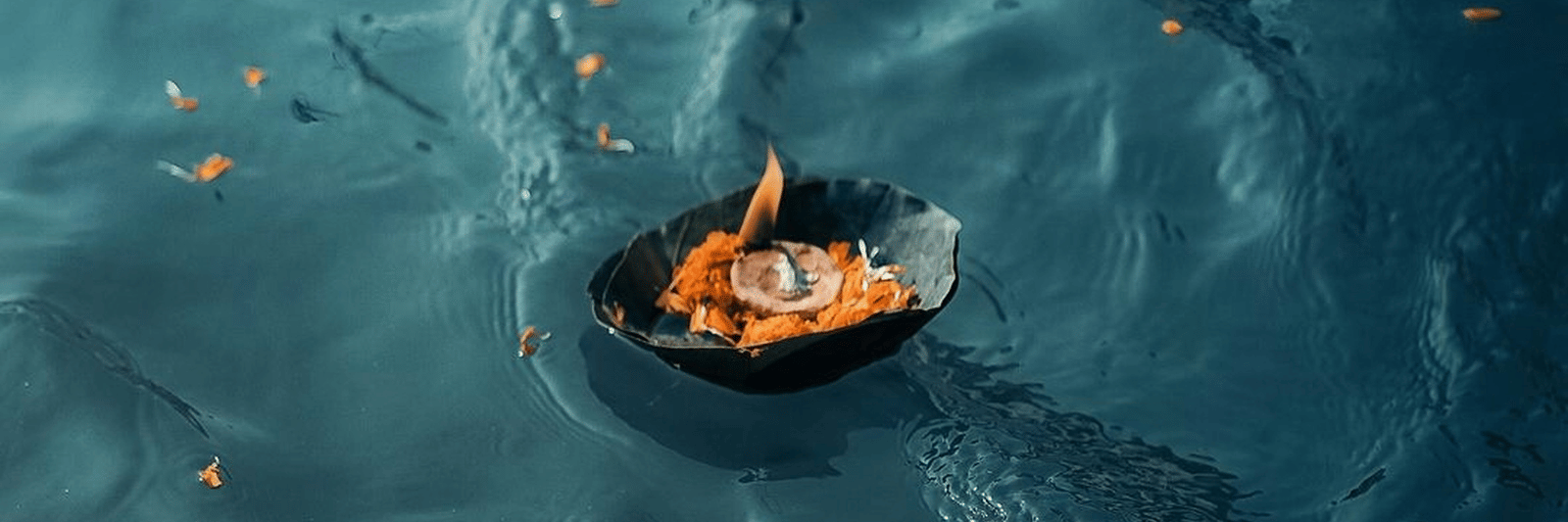 A small lamp with a lit offering floats on a calm, dark blue body of water.