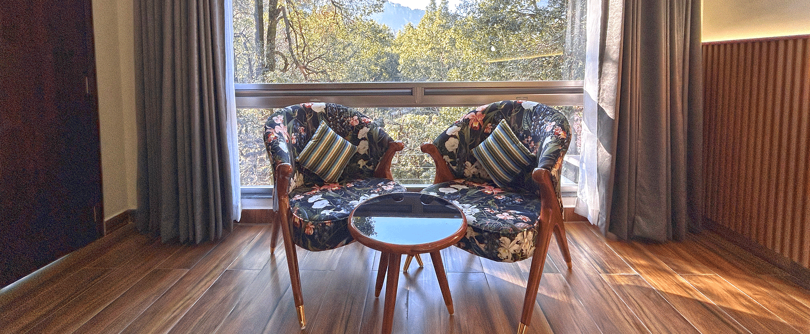 A close up shot of two chairs and a coffee table with a large window through which sunlight is beaming into the room - DLS The Emerald, Nainital