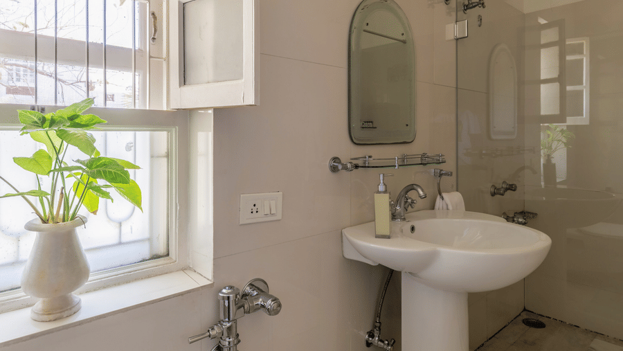 Bathroom with a white pedestal wash basin, a mirror, and a small window with natural light at Barwara Kothi, Jaipur.
