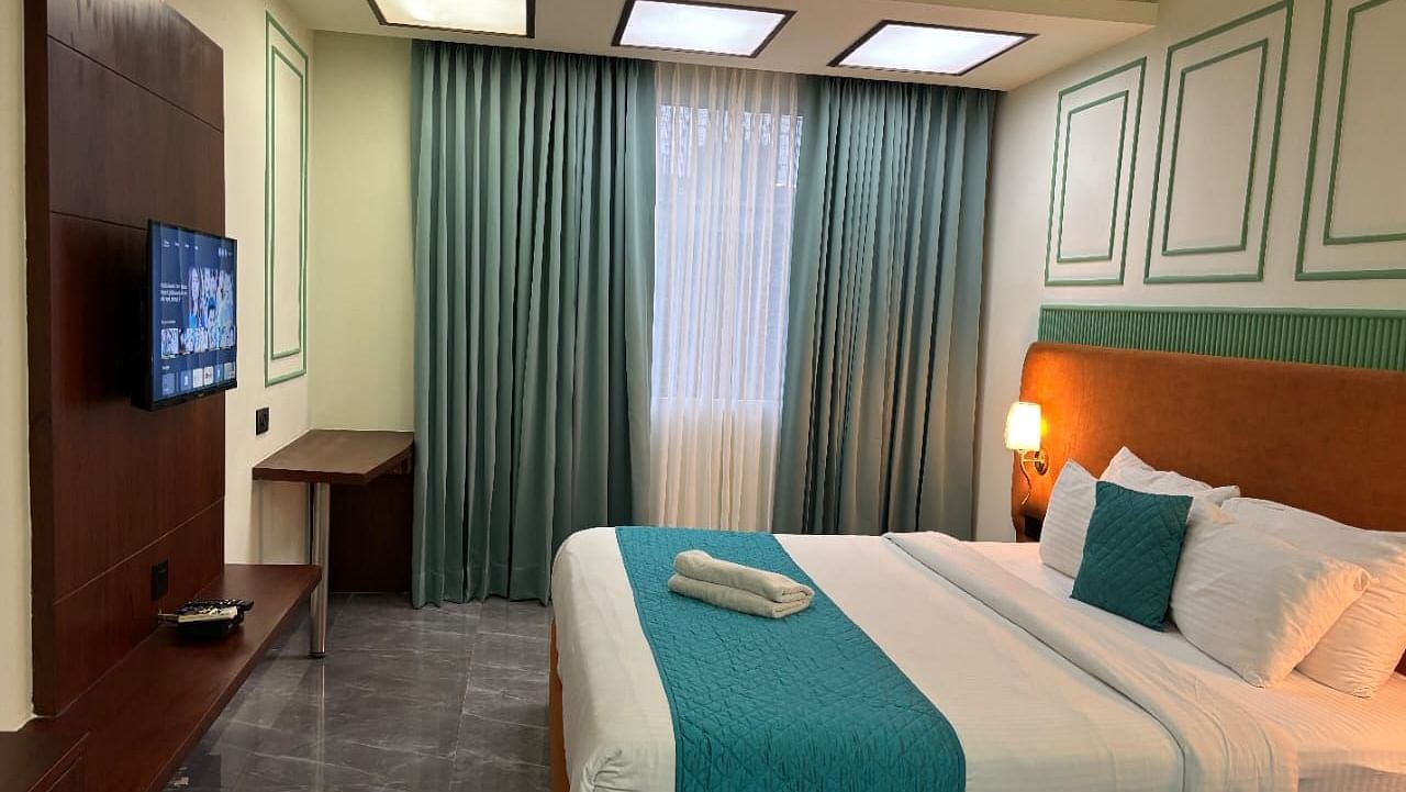 A comfortable room showing a double bed with blue accents, a television, and curtains - Asian Suites IFFCO Metro, Gurgaon