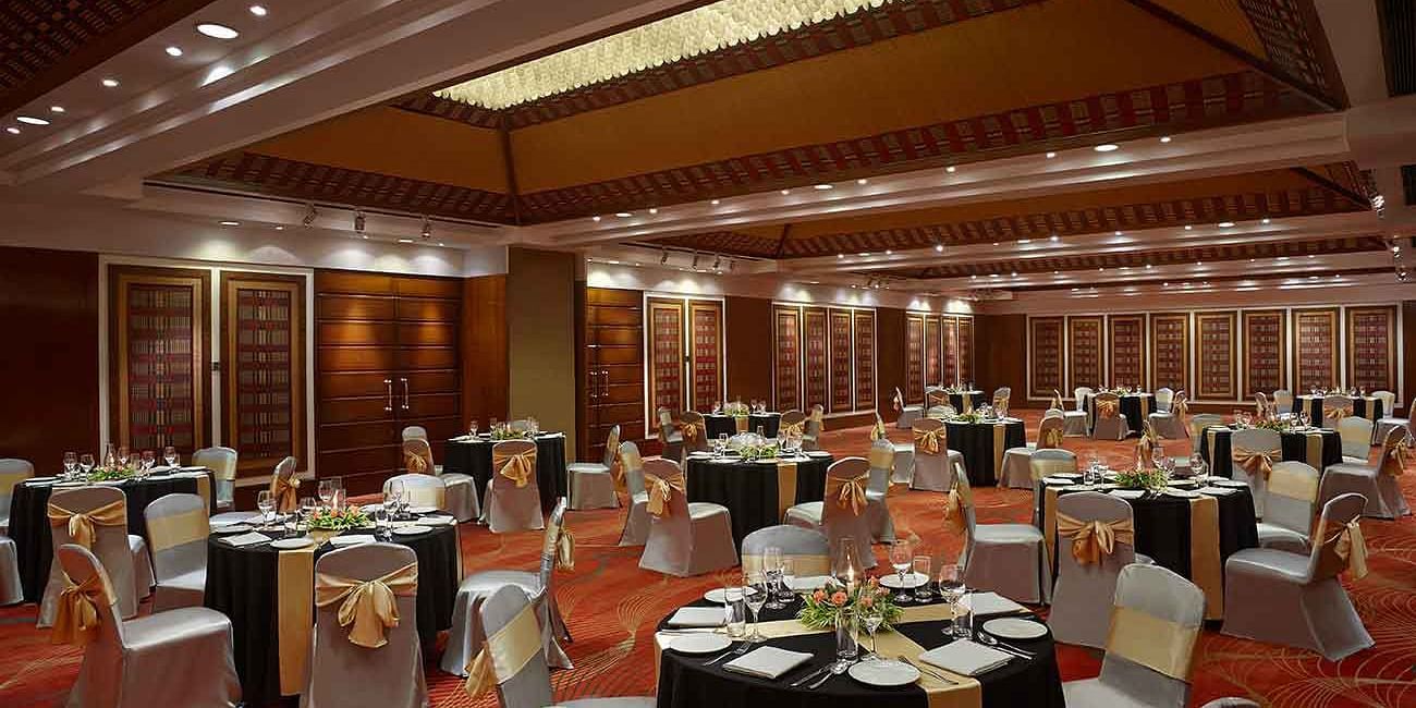 A spacious banquet hall set up with round tables, chairs adorned with bows, and elegant table settings.