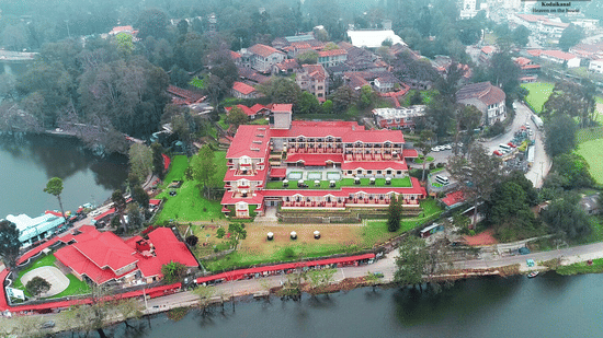 Aerial view of The Carlton Kodaikanal with red-roofed resort buildings, lush greenery, and a serene lake surrounding the property.