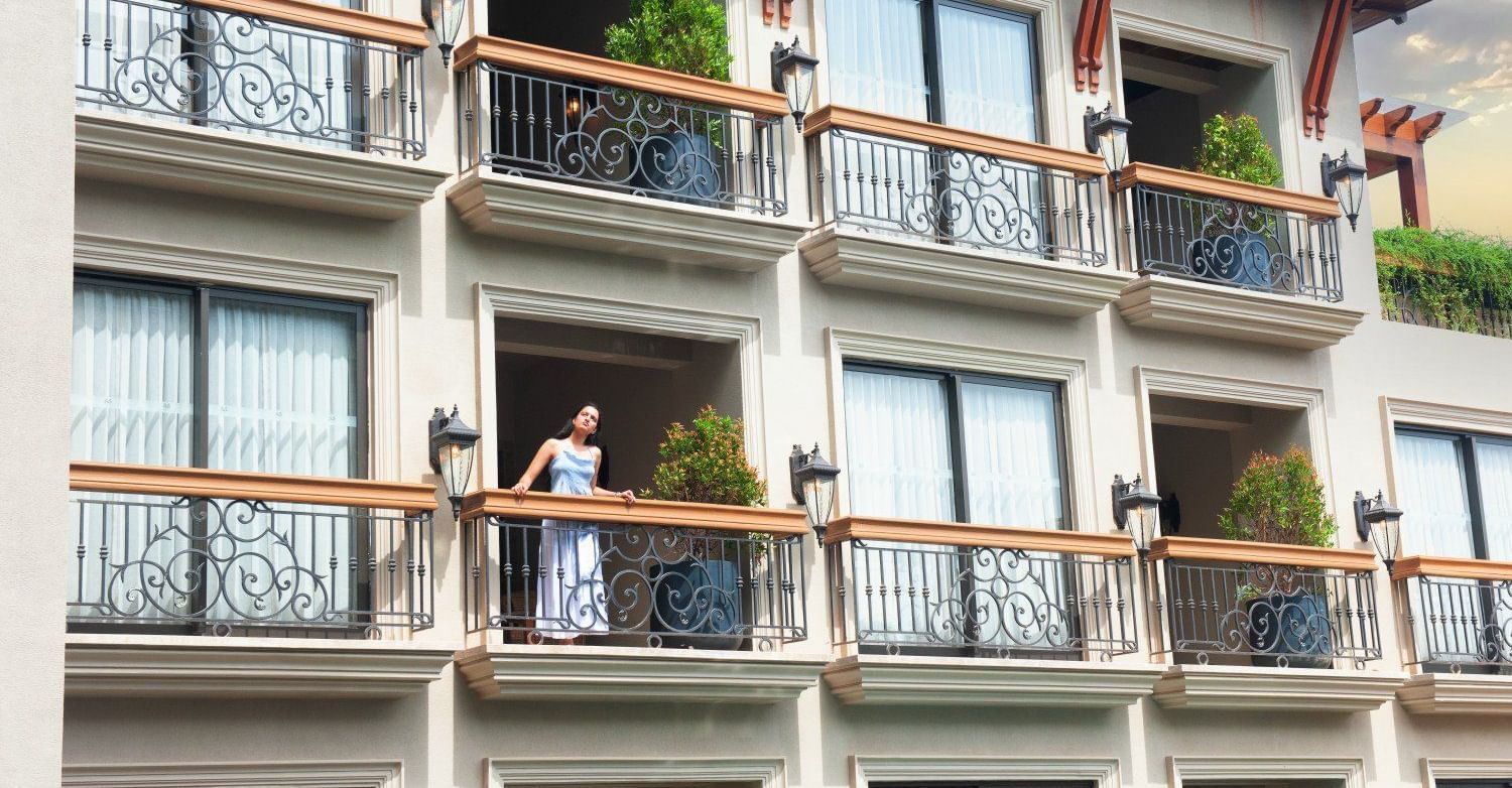 A woman standing in the balcony looking at the surrounding as she leans against the railing at The Evren, Vagator.