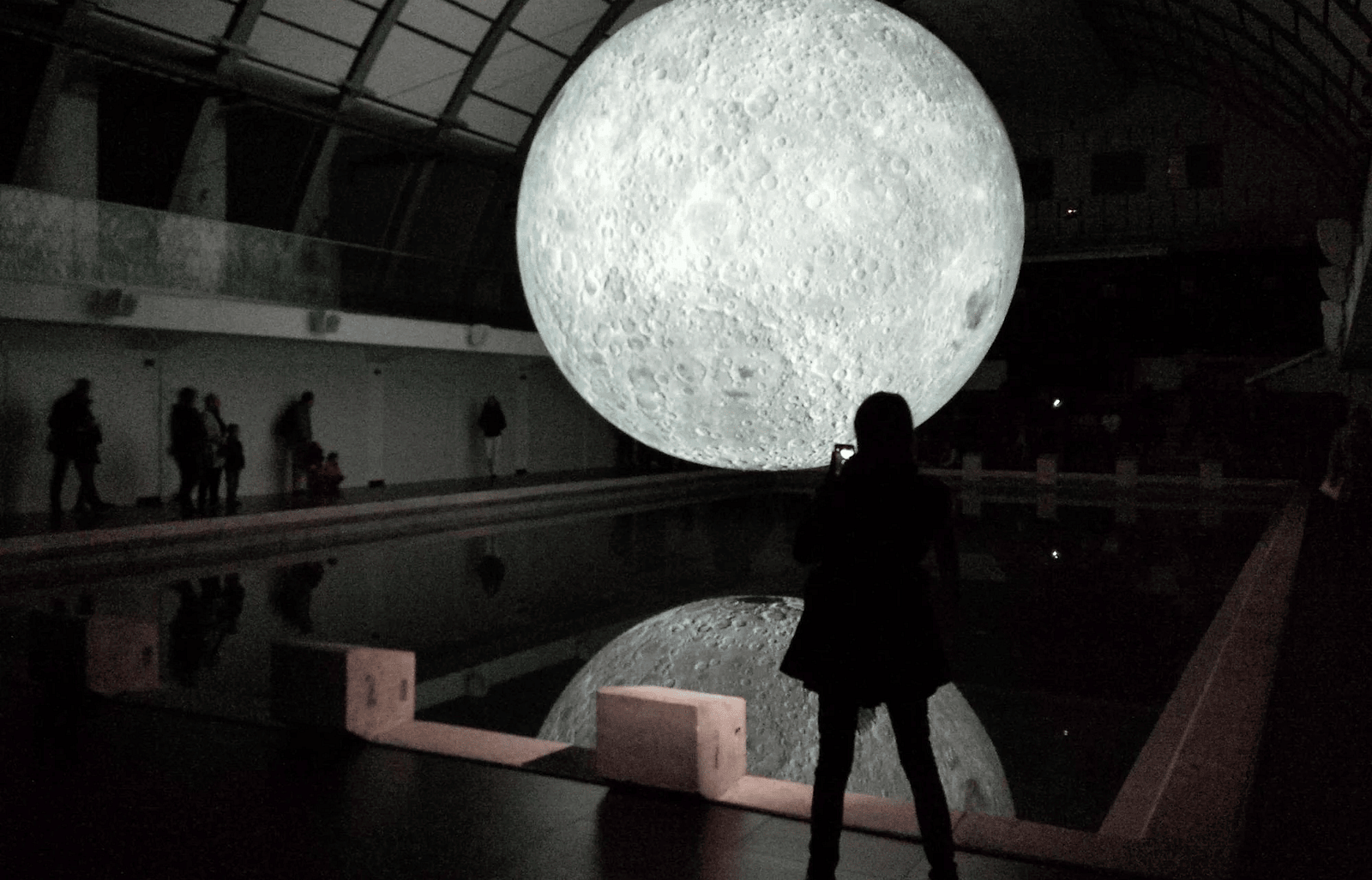 An image of many individuals at a planetarium  and one person is staring at huge clone of a moon